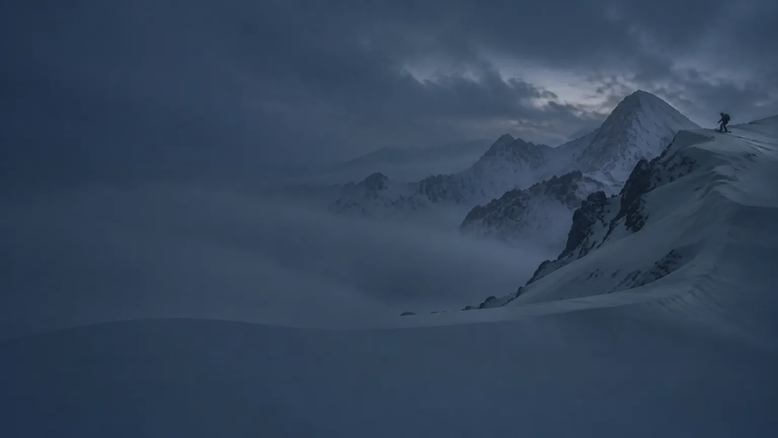 A snowboarder traversing a high alpine ridge at blue hour
